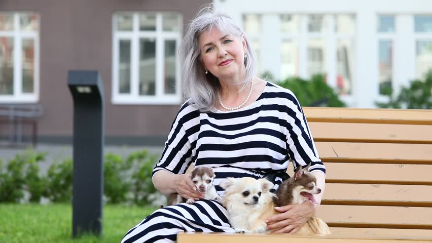 Elderly woman sitting on a bench with her pet dogs