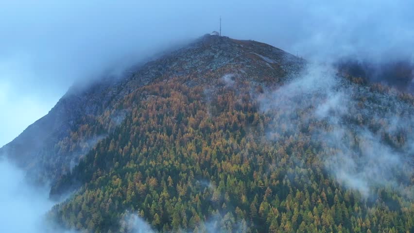 Saastal Saas Fee Switzerland aerial drone mountain larch forest peak moody clouds layer gray grey rainy fog mist Swiss Alps mountain peaks glacier valley pole weather station to the right motion