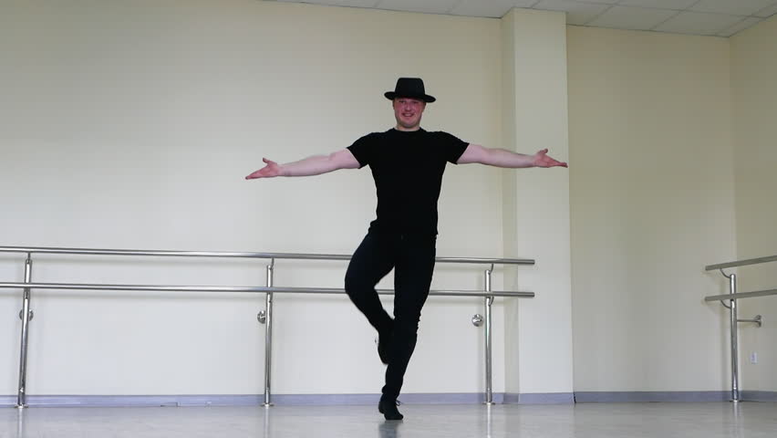 Jazz dance or caberet rehearsal in the studio by a young guy in a gangster hat. Creative dance blues mena. Dancer in black clothes against the background of a mirror in reflection