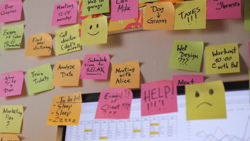 Close-up of female worker adds bright sticky notes to a wall covered in reminders while working on computer late in the evening. Time organization and planning