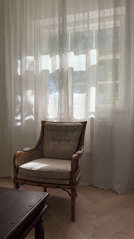 Lovely bright morning sun shining in from a window of elegant luxury living room with beige brown linen natural curtains behing an vintage rattan antique chair floral pattern fish tail floor interior 