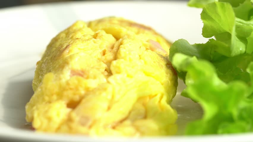 A plate of food with a yellow omelet and a green leafy vegetable. The plate is white and the food is arranged neatly