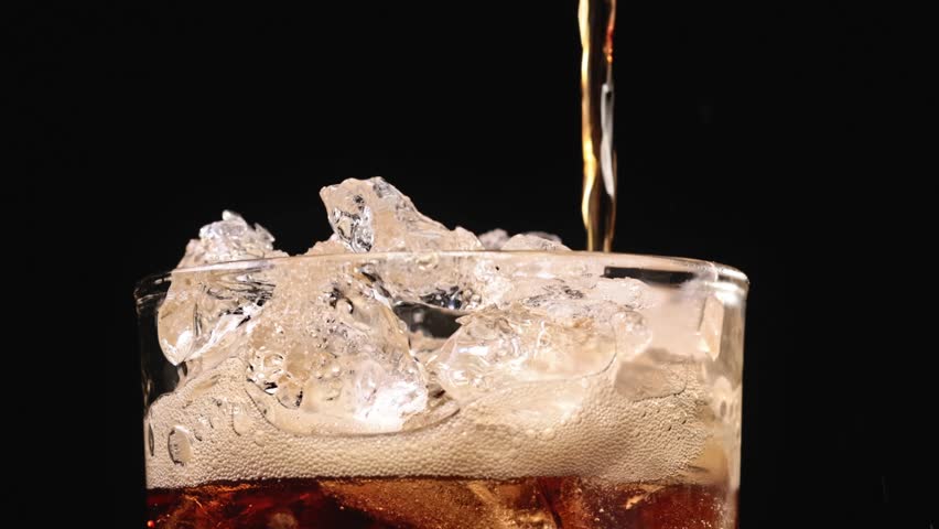 Closeup of pouring cola drink with ice cubes. Fizzing cola with ice in glass. Refreshing tasty cola drink.