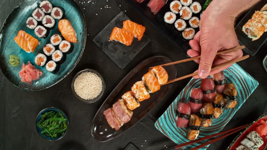 Top view of traditional japanese cuisine . Sushi rolls set with salmon , tuna fish and vegetable served on black stone table . Asian food on black stone slate with chopsticks . Camera movement .