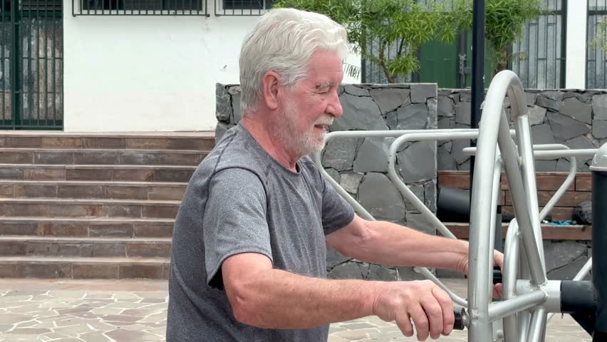 Active smiling retired man exercising outdoors with sports free equipment to keep fit. Cardio and muscle exercises for mature people. Athletic spirit concept