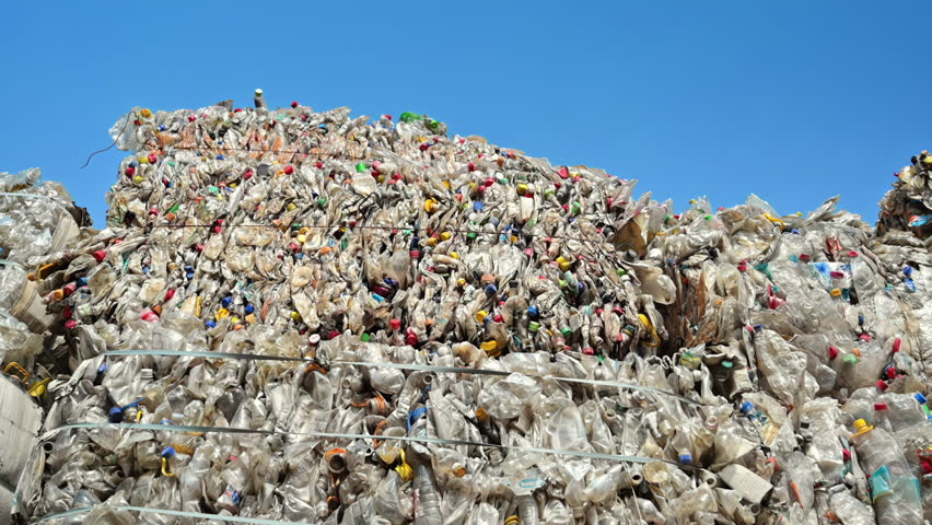 Multiple stacks of compressed transparent plastic garbage at waste recycling factory in open air. Slow motion