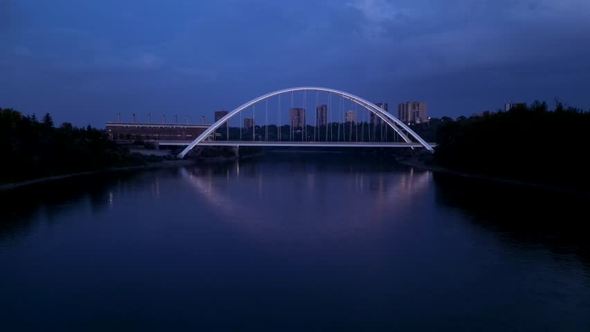 A drone flying over the North Saskatchewan River towards Walterdale Bridge at a cloudy sunset in Edmonton, Alberta, Canada