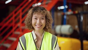 Cheerful warehouse worker wearing a safety vest, standing in an industrial setting with red stairs and equipment in the background. - Powered by Shutterstock - Get 15% off with code: PIKWIZARD15