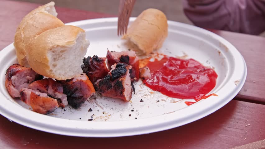 Delicious Unhealthy Grilled Sausage Served with Bake Roll and Tomato Ketchup on Disposable Paper Plate during Outdoor Picnic Event
