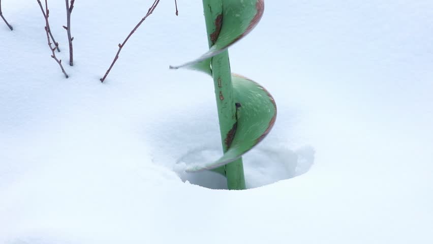 Green manual ice auger drilling into the snow-covered ice, creating a fishing hole in winter landscape winter