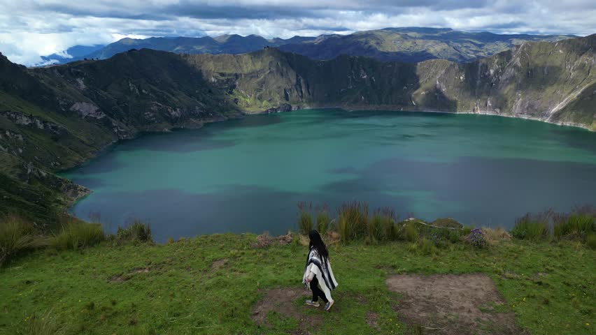 young Latina in poncho exploring Quilotoa volcano lake slope (3,914 m) Aerial drone view