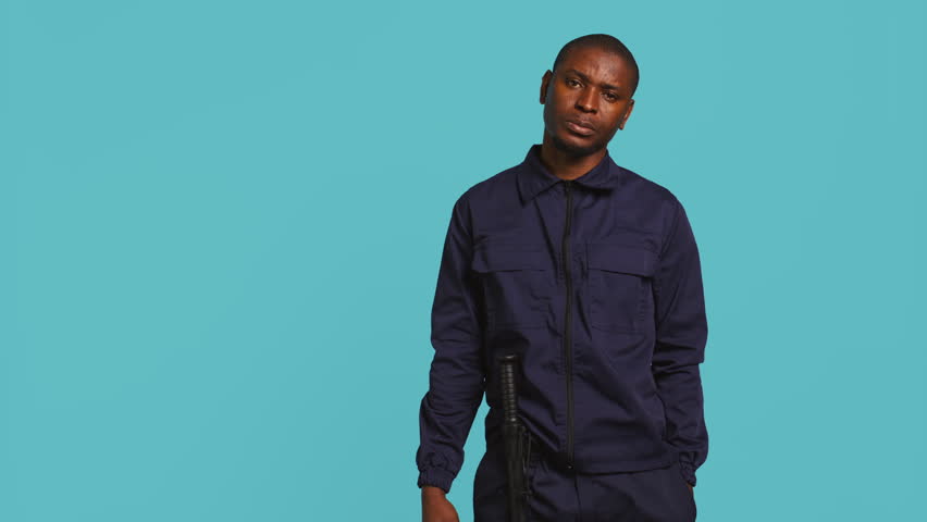 Security guard holding clock, rushing people out of property. Portrait of stern bodyguard showing visitors time is passing, preparing for closing down location, studio background, camera B