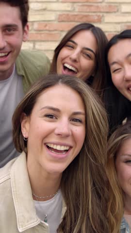 Vertical video. Happy group of young friends smiling at camera outdoors. Portrait of multiracial student people having fun together. Friendship concept.