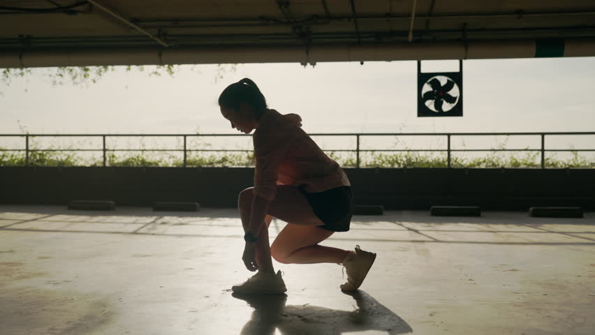 A woman is doing a workout in a parking lot. She is wearing a red shirt and black shorts