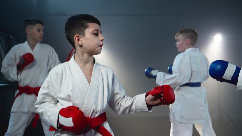 Focused kids training karate and practice fight technique. Males in white kimono sparring. Healthy kids. Smoky background with spotlights. Boys practicing karate. F4K, UHD