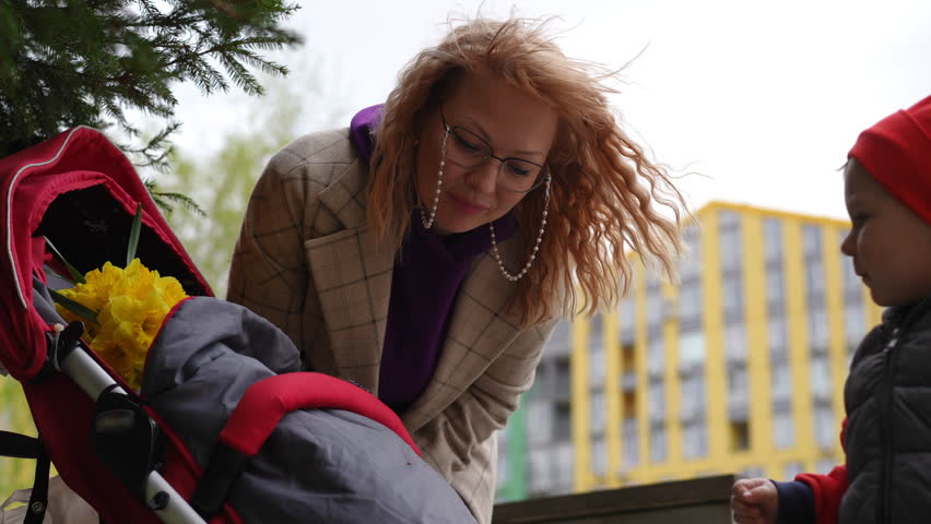 Slow motion. A mother shows a ladybug sitting on a baby stroller to her little son. A mother and child examine a beetle, while standing outdoors under the trees on a spring day in the courtyard of a
