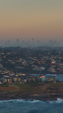 A vertical drone footage of the cityscape of Sydney as seen from Maroubra Beach at sunset in New South Wales, Australia