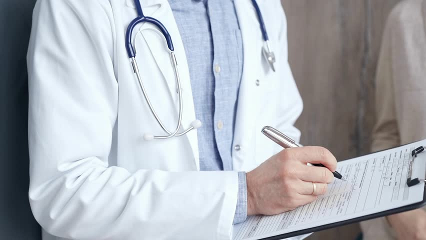 Healthcare professional doctor is focused on updating medical charts on a clipboard. Male unrecognizable physician at work. Medicine and pharmacy