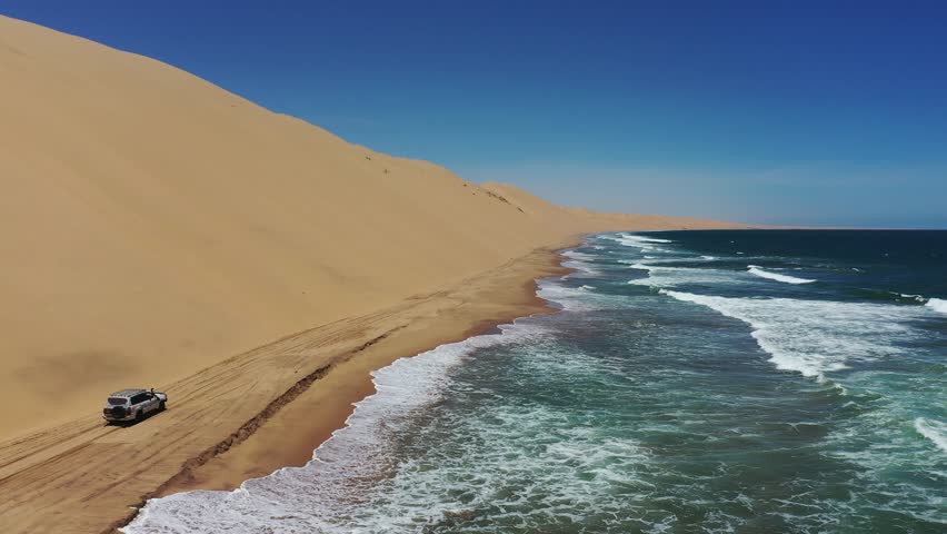 A drone footage of a car drive of a sandy road along the Atlantic Ocean coast in Sandwich Harbour Historic, Walvis Bay city, Namibia