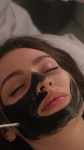 Carbon peeling of the face of a young beautiful girl. Skin care cosmetology. Laser therapy and skin treatment. Vertical video.