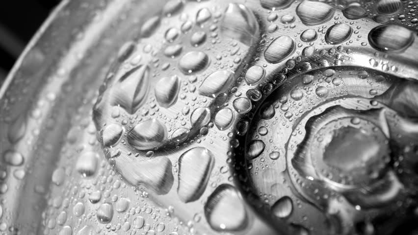Detailed close-up showcases the top of an aluminum beverage can, adorned with tiny water droplets, accentuating the tactile feel of its ridges and the visibility of its tab. Can background.
