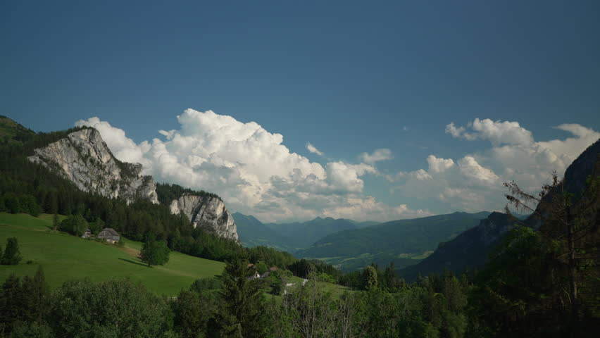 Beautyful wide angle shot of mountains and green meadows with big fluffy clouds in the background in mild sunlight. Good background for graphics