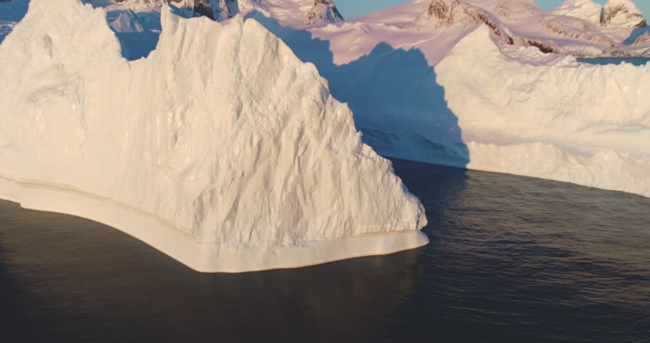 Huge iceberg floats Antarctic waters in sunset light, aerial drone footage. Breathtaking scene of Antarctica glacier ice wall, mountains in background. Cinematic ecology scene. Zoom out panorama