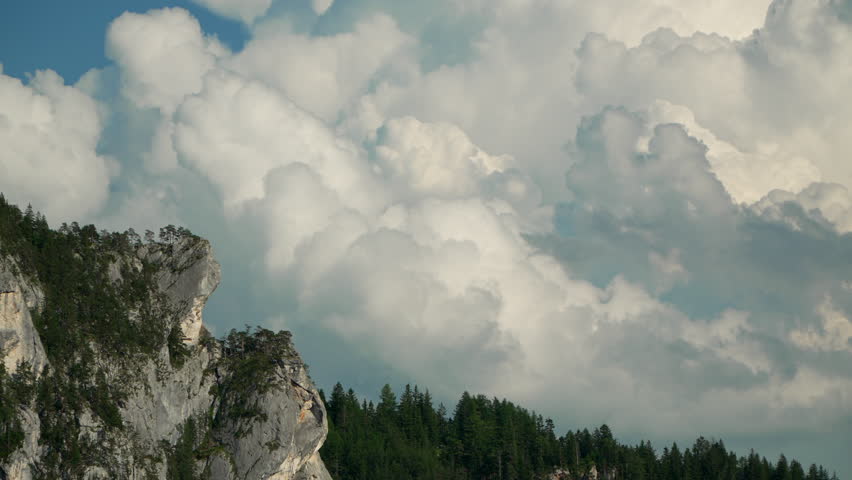 Beautyful fluffy clouds in dramatic light passing slowly behind rock formation.