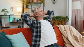Tired senior man with gray hair in casual clothes stretching arms and resting on sofa in living room. Thoughtful Caucasian middle-aged guy relaxing on couch with hands behind head looking away at home - Powered by Shutterstock - Get 15% off with code: PIKWIZARD15