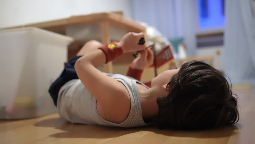 Child lying on the floor, carefully examining a toy, absorbed in imaginative play, enjoying a peaceful moment of creativity