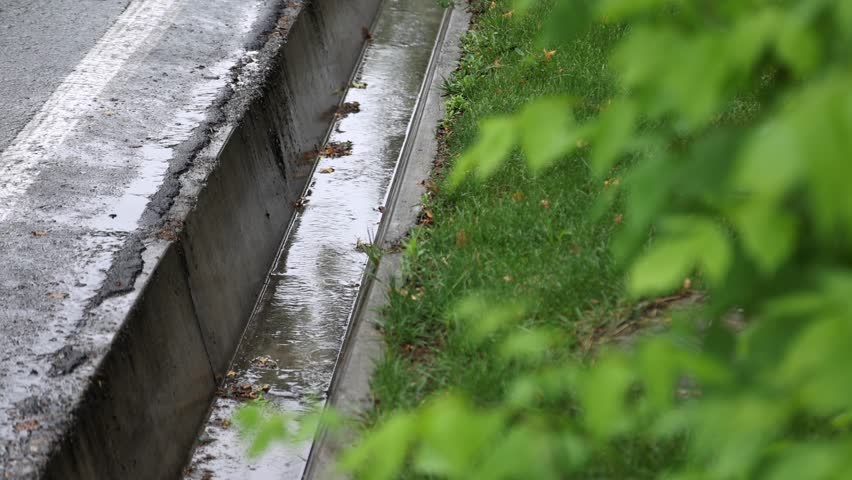 Raindrops in the gutter on the side of the street. High quality 4k footage.