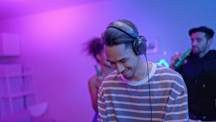 Group of diverse man and woman dancing with DJ mixing music on console. Attractive young teenager friends having fun with DJ mixing and scratching music mixer controller at house party with neon light