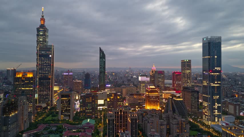 Aerial hyperlapse at dusk above Downtown Taipei, vibrant capital of Taiwan, with 101 Tower standing out amid skyscrapers in XinYi Commercial District and city lights dazzling under moody twilight sky