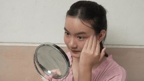 A young Asian woman in a pink dress sits on the front house stairs, holding a mirror and looking at her own face, enjoying a moment of self-reflection and beauty. - Powered by Shutterstock - Get 15% off with code: PIKWIZARD15