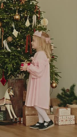 Family Christmas Traditions. Two happy little girls sisters giving presents and hugging in the background of the Christmas tree. Happy family. Happy new year. Cinematic slow motion.
