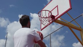 Young man shooting basketball towards hoop during outdoors game. Basketball court under cloudy blue sky highlighting training or competitive session. Concept of spirit of sports and recreation. - Powered by Shutterstock - Get 15% off with code: PIKWIZARD15