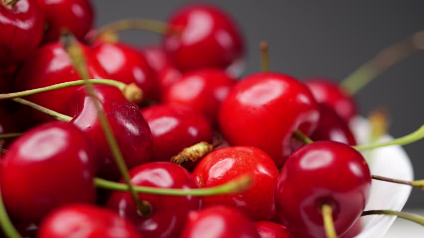 Fresh cherries rotate on a white plate. Juicy fruits against a dark backdrop, macro views. Promoting healthy nutrition and a vegetarian diet. Well-lit, appetizing presentation.
