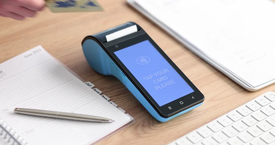 Woman pays with credit card and wireless terminal in office slow motion. Contemporary technology of banking service. POS machine on desk