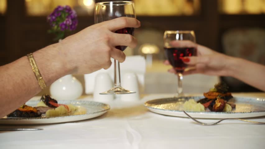 Young couple in love having dinner in restaurant drinking red wine clinking glasses while sitting at table with candles and dishes celebrating Valentine
