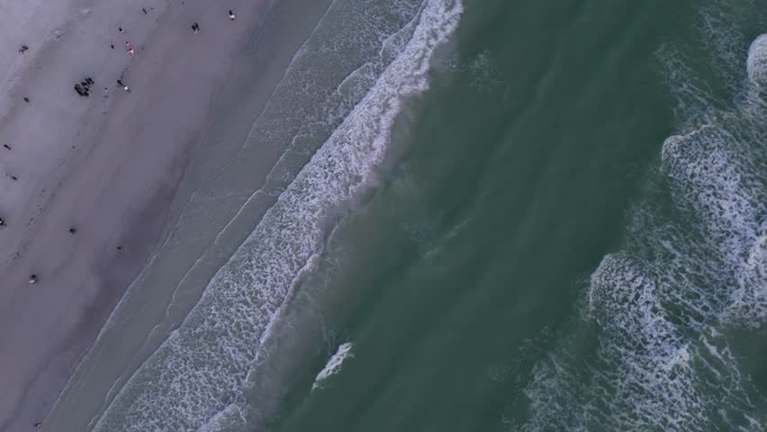 An aerial view of the Atlantic Ocean waves on Siesta Beach, and the coastal buildings at sunset in Siesta Key city, Florida, United States