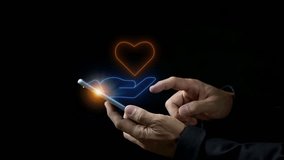 Healthcare, love, organ donation, mindfulness, wellbeing, insurance and praying concept. Businessman hand holding smartphone to show glowing neon line of hand holding heart icon on virtual screen. - Powered by Shutterstock - Get 15% off with code: PIKWIZARD15