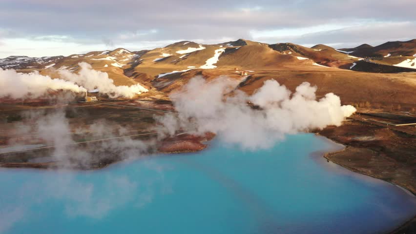 Geothermal heat stations in Iceland, clean energy of the Earth. Drone video through clouds of blue lake near terrain and mountains. Iceland, north-eastern region.