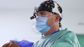 Caucasian doctor wearing cap, mask, protective goggles and headlight looks ahead. Close up side view portrait of a surgeon operating and looking at the screen. - Powered by Shutterstock - Get 15% off with code: PIKWIZARD15