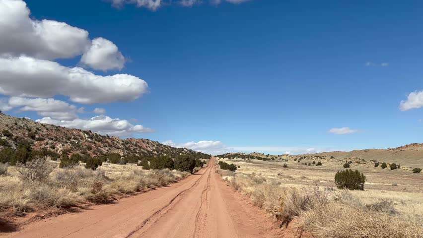 Point of View POV driving down a rutted red dirt road in Capitol Reef National Park known as the Burr Trail Road. The road continues into the distance with a beautiful blue sky - Utah, USA