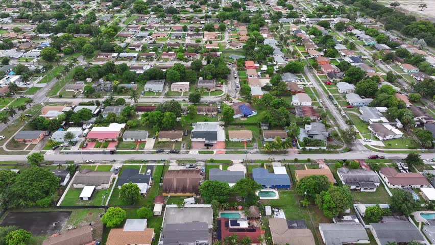 American neighborhood in quaint suburb of Miami City during sunny day in summer. Green trees on street in noble housing area with Swimming pool in garden. Aerial birds eye shot.