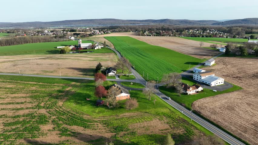 Drone flyover farm house with silo surrounded by cultivation fields in american countryside. Sunny day in the evening. Car on rural road in suburb.