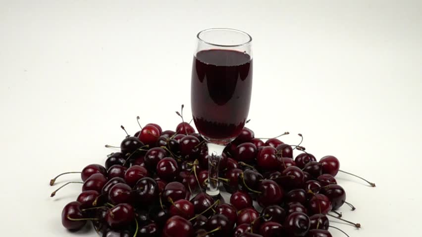 Ripe fresh cherry fall into a wineglass with red  wine standing among cherries, slow motion