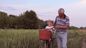Cheerful child riding bike with her grandfather in green field family enjoying active outdoor relaxation looking around at beautiful nature senior man spending time with his grandchild on green meadow - Powered by Shutterstock - Get 15% off with code: PIKWIZARD15