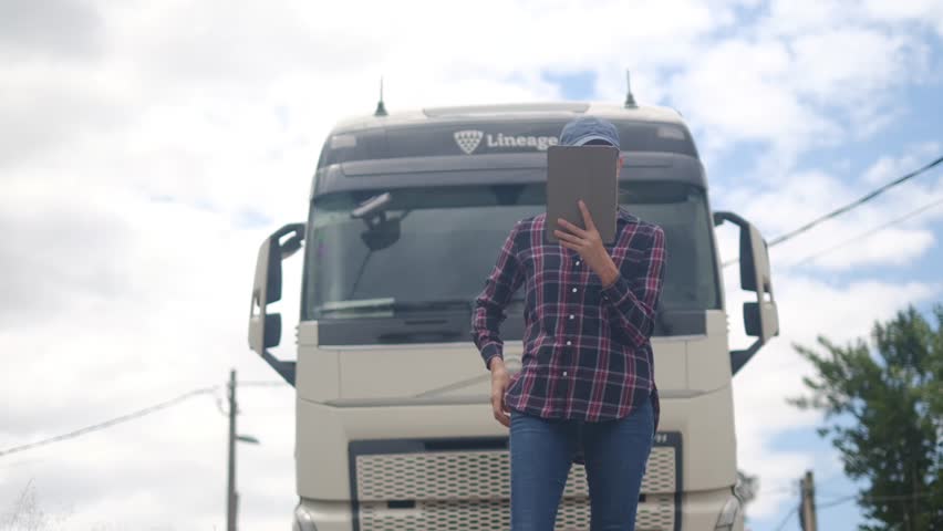 Female truck driver with digital tablet controlling the route and checking merchandise to transport. Gender equality and entrepreneurial women in logistics and transportation