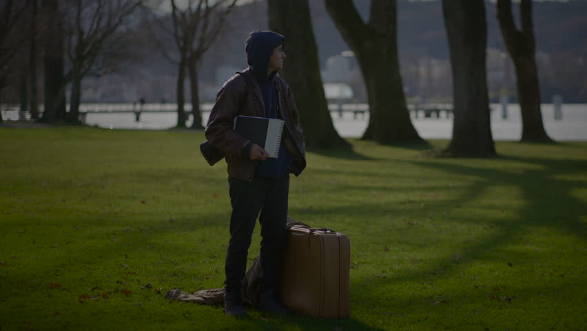 A man seated beneath the verdant canopy of the park and sketching through his paper